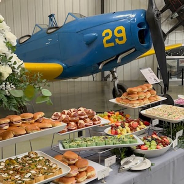 Martiniz Fresko Kitchen brunch buffet with sliders, fruit, and appetizers, set against a blue airplane.