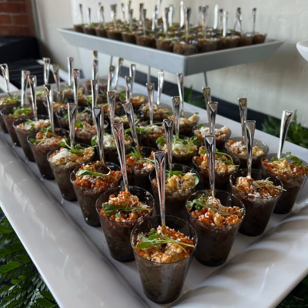 Numerous small cups of Martiniz Fresko Kitchen's brunch appetizers with spoons on a tiered serving tray.
