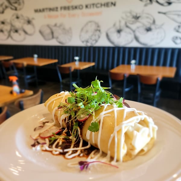 Martiniz Fresko Kitchen's brunch burrito, drizzled with sauce and topped with fresh greens, on a white plate.
