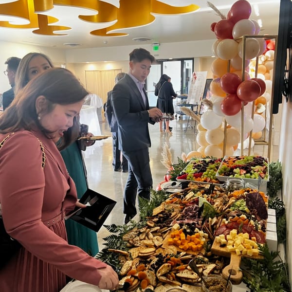 Guests gather around a lavish brunch buffet featuring fruit, cheeses, meats, and crackers at Martiniz Fresko Kitchen.