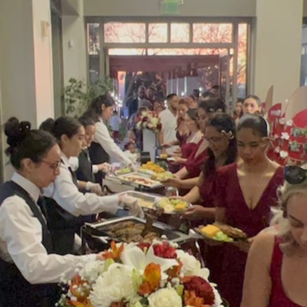 Guests in red dresses and servers in black vests line up for a brunch buffet at Martiniz Fresko Kitchen.