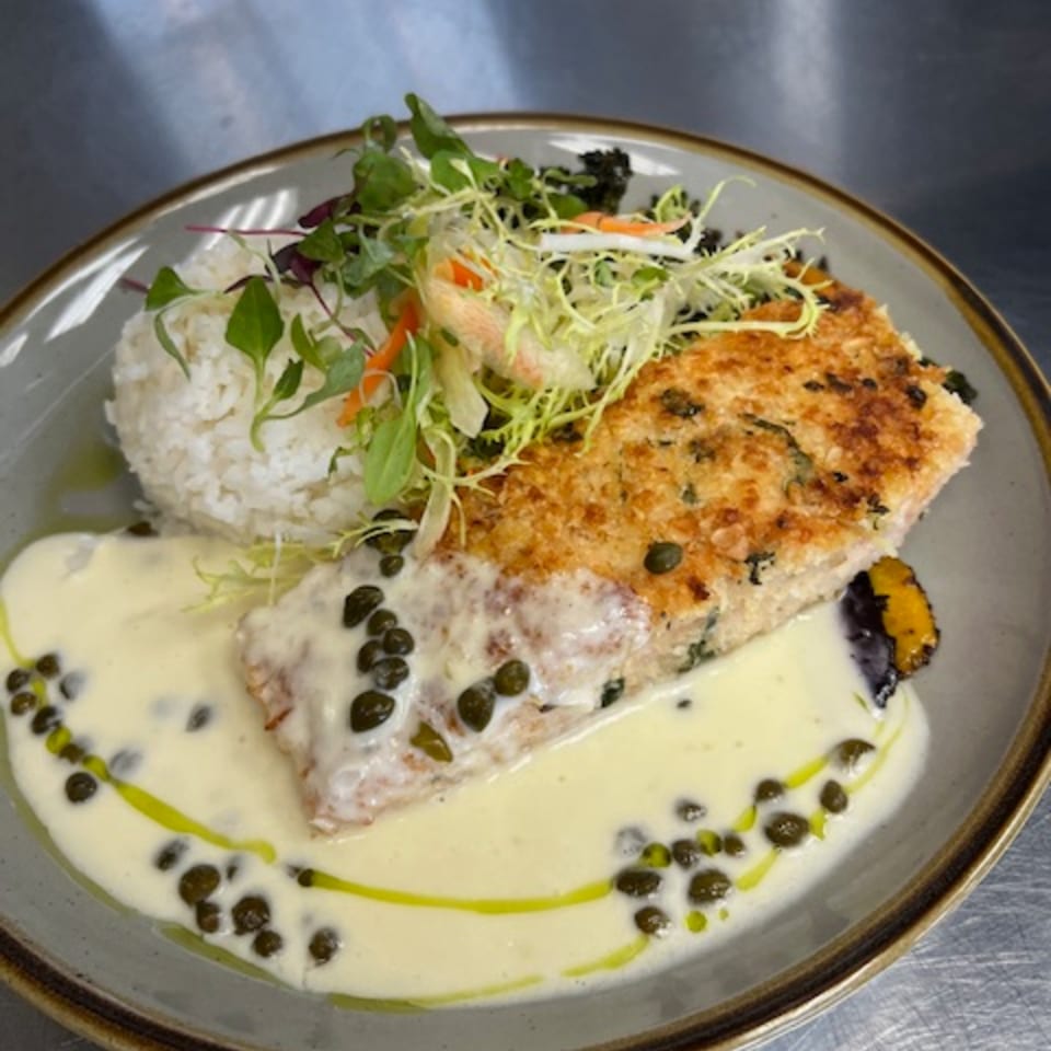 Crispy salmon with caper cream sauce, white rice, and fresh greens on a plate.