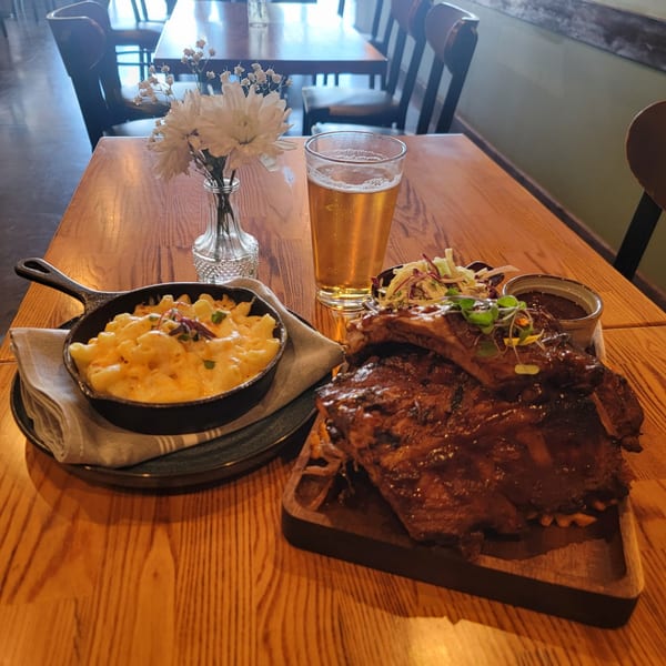 Martiniz Fresko Kitchen's ribs, mac and cheese, coleslaw, and beer on a wooden table.