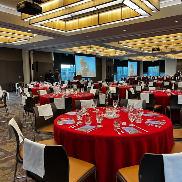 A large event room with multiple round tables covered in red tablecloths, set for dining.