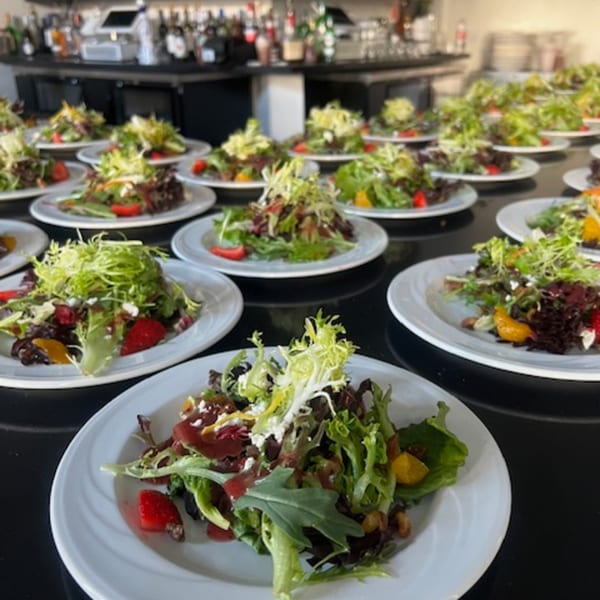 Numerous fresh Martiniz Fresko Kitchen salads with mixed greens, fruit, and cheese on white plates.