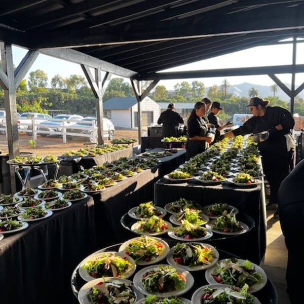 Martiniz Fresko Kitchen staff preparing many fresh salads on long tables outdoors for a brunch event.